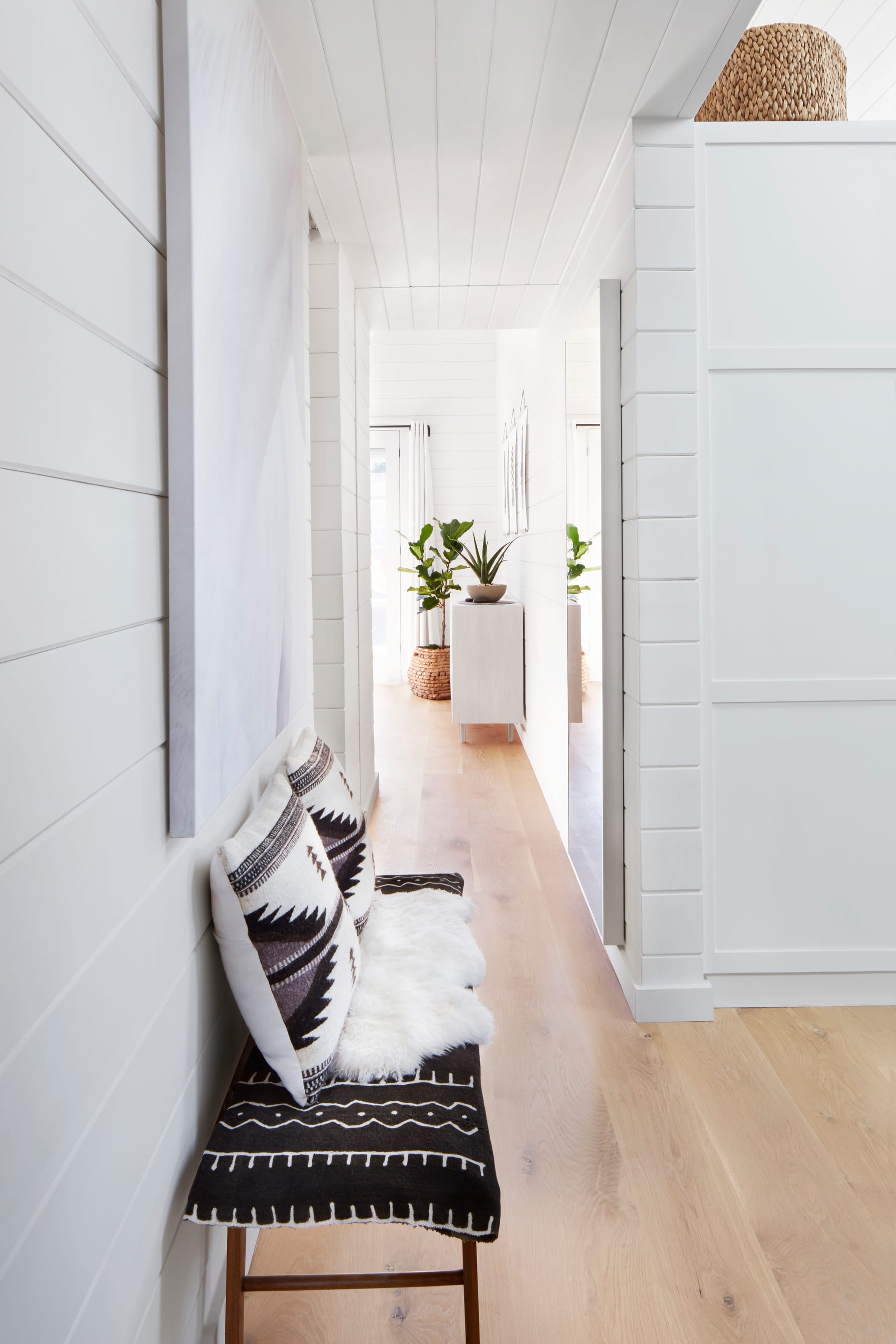 Bright white shiplap hallway with a patterned bench and potted plants