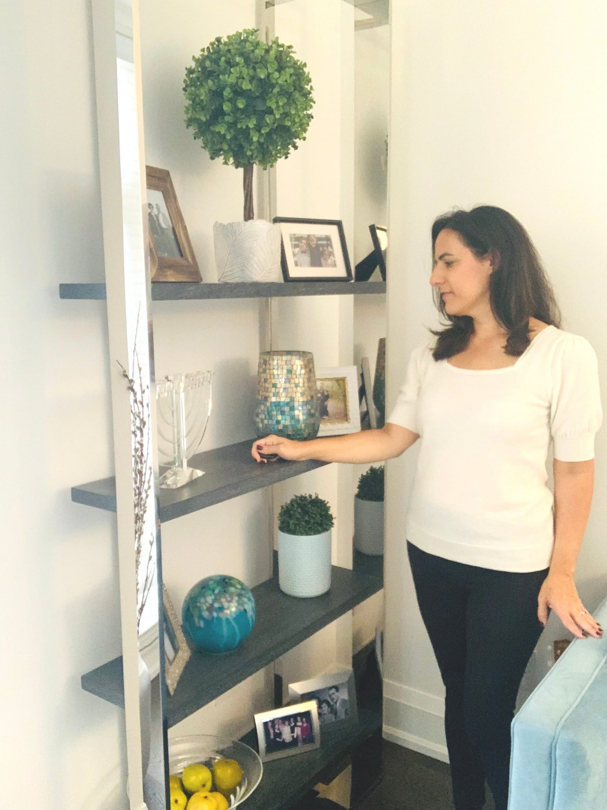Home organizer styling a shelving unit with plants and framed photos