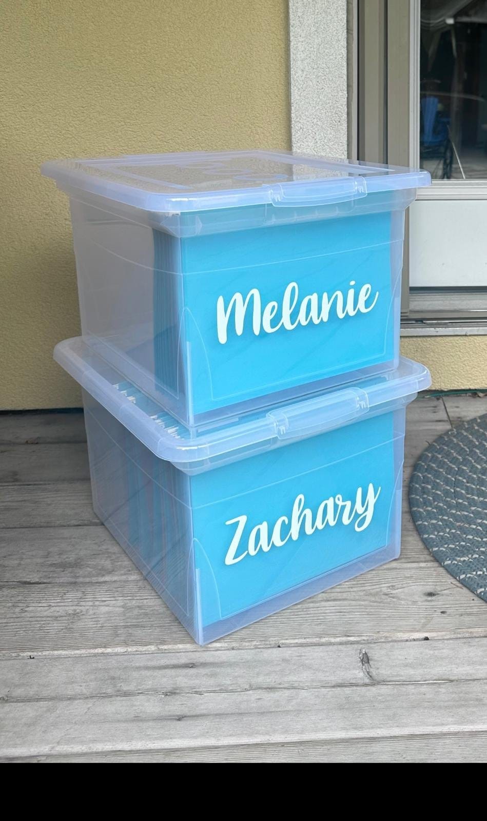Two clear memory bins labelled Melanie and Zachary on a porch