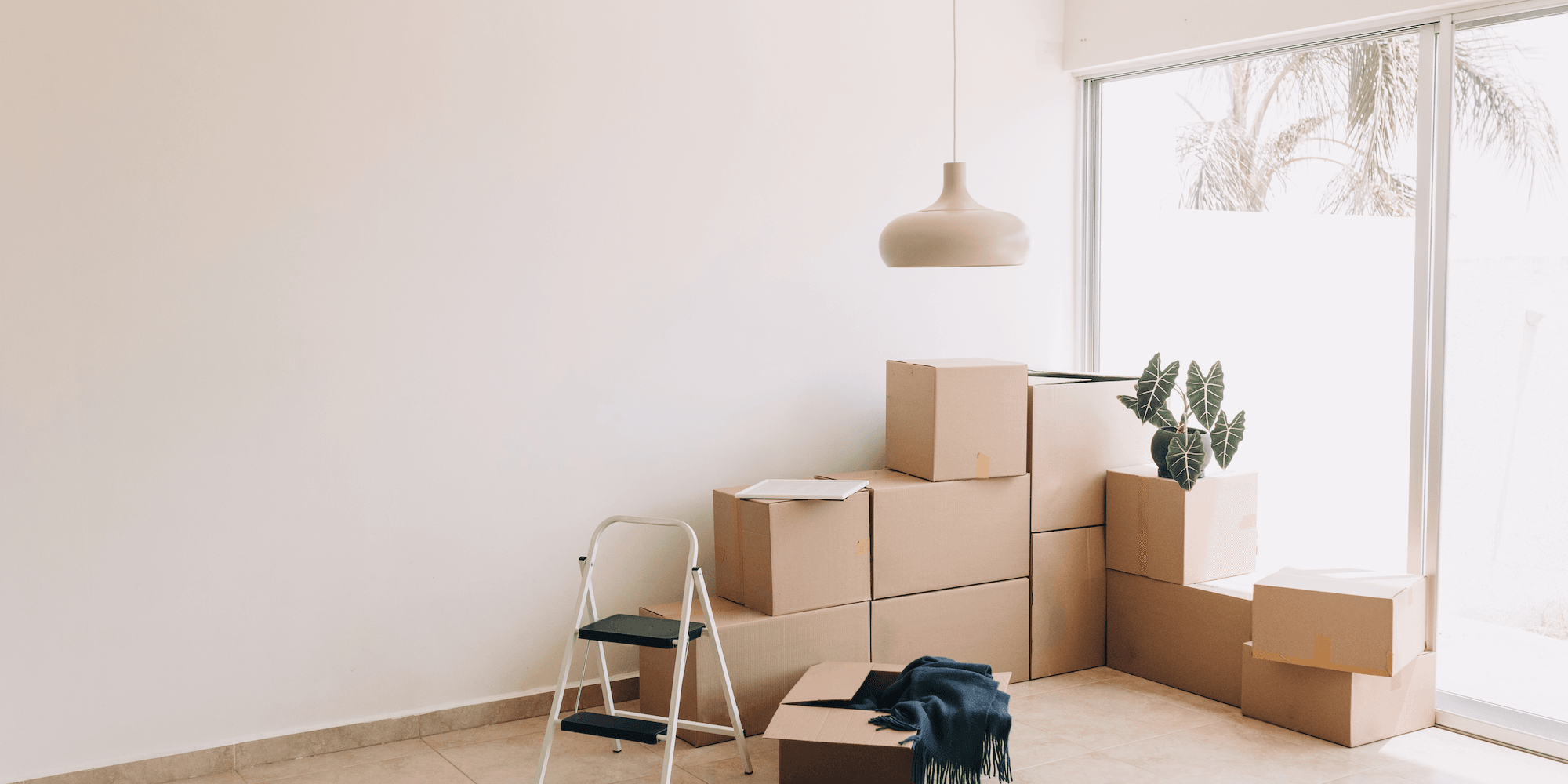 Stacked moving boxes and a step stool in a bright empty room