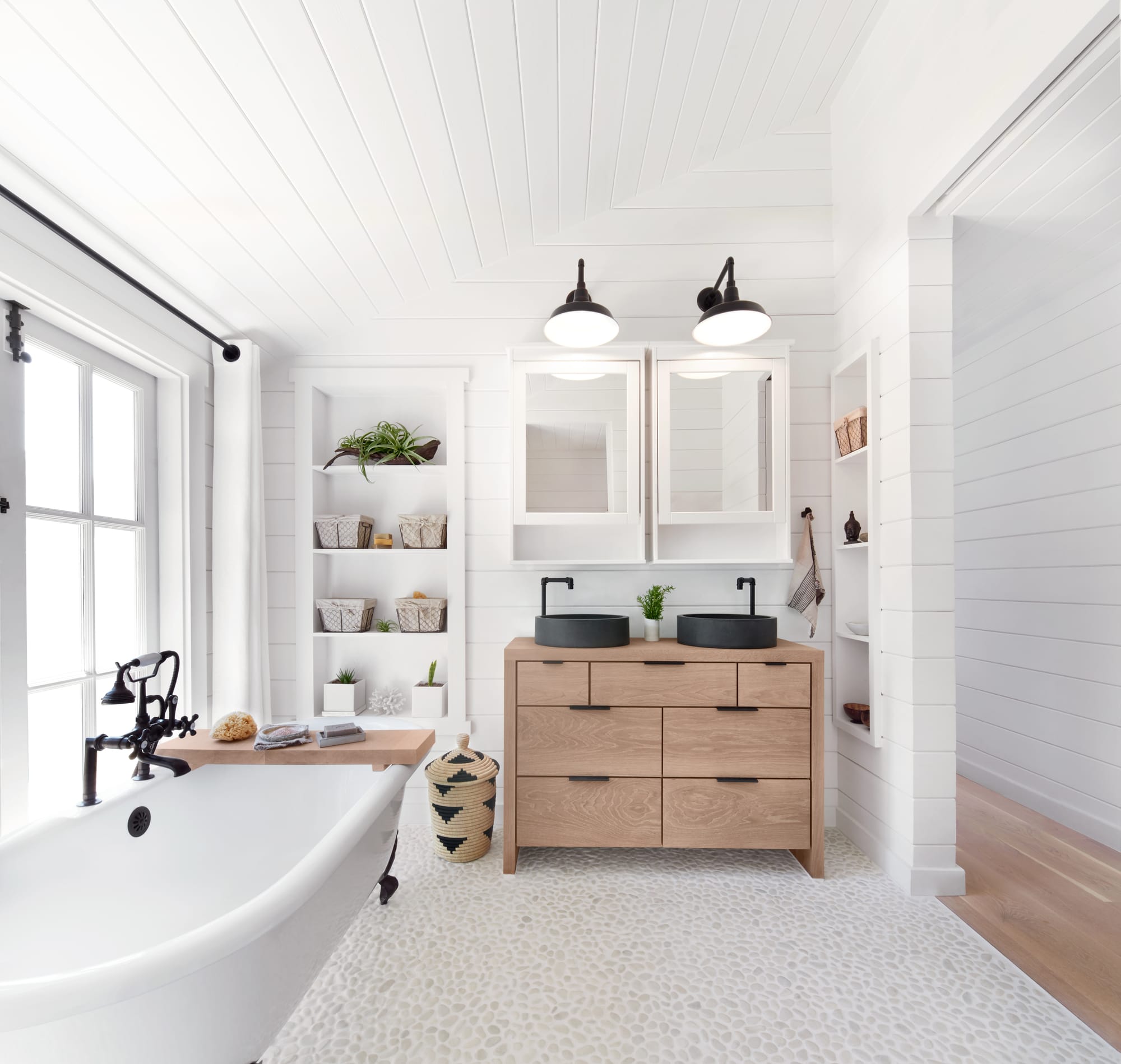 Bright white farmhouse bathroom with a wood vanity and styled shelving