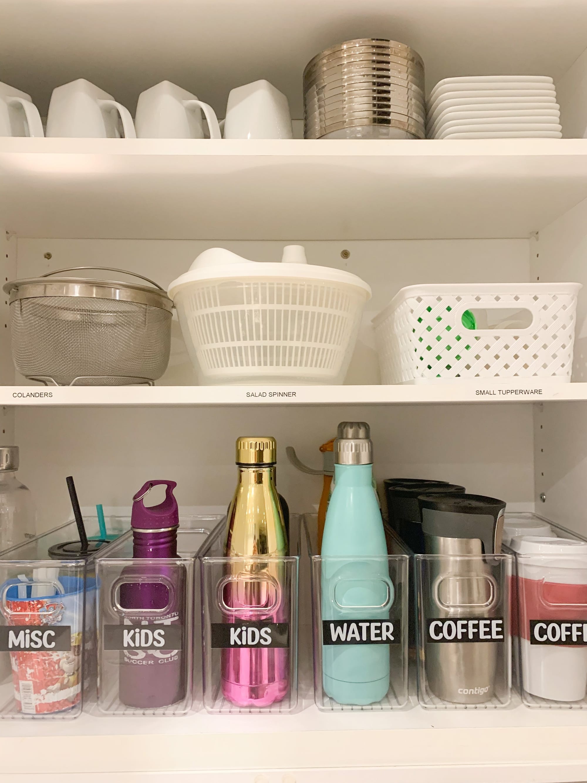 Organized kitchen cabinet with labelled bins for water bottles and mugs