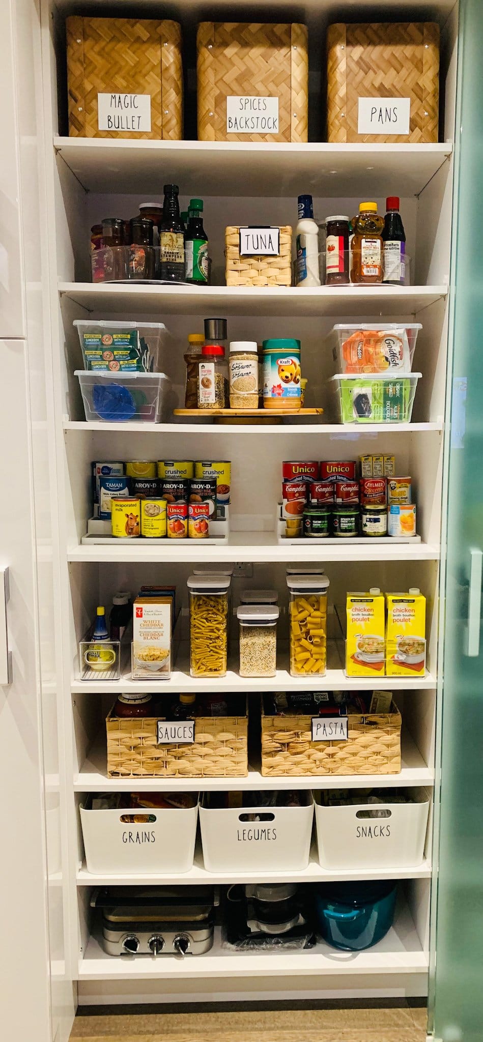 Well-stocked white pantry with woven and labelled bins on every shelf