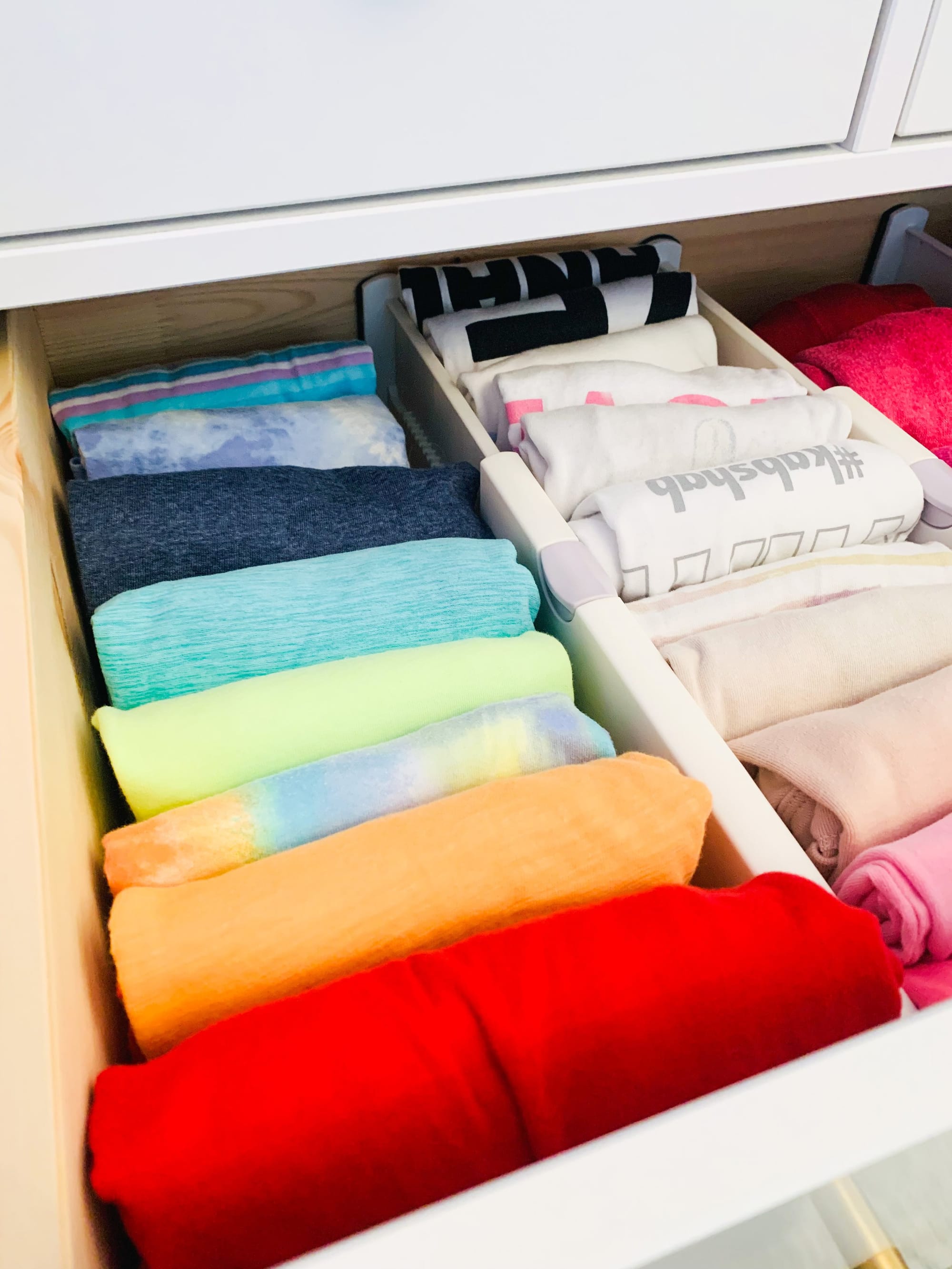 Drawer of rainbow file-folded clothing separated by dividers