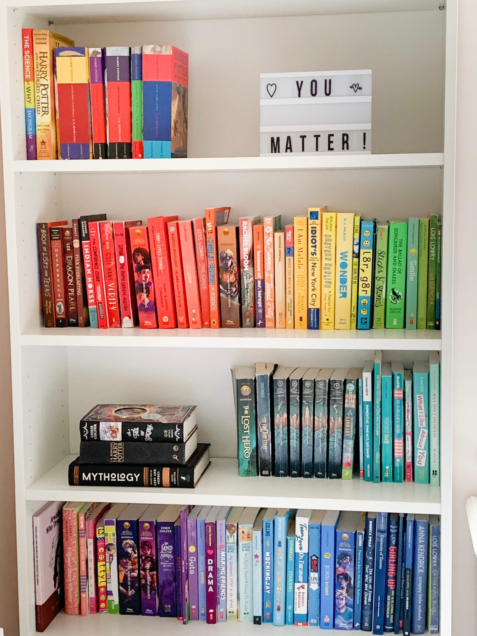 Kids bookshelf organized by rainbow colour with a You Matter sign