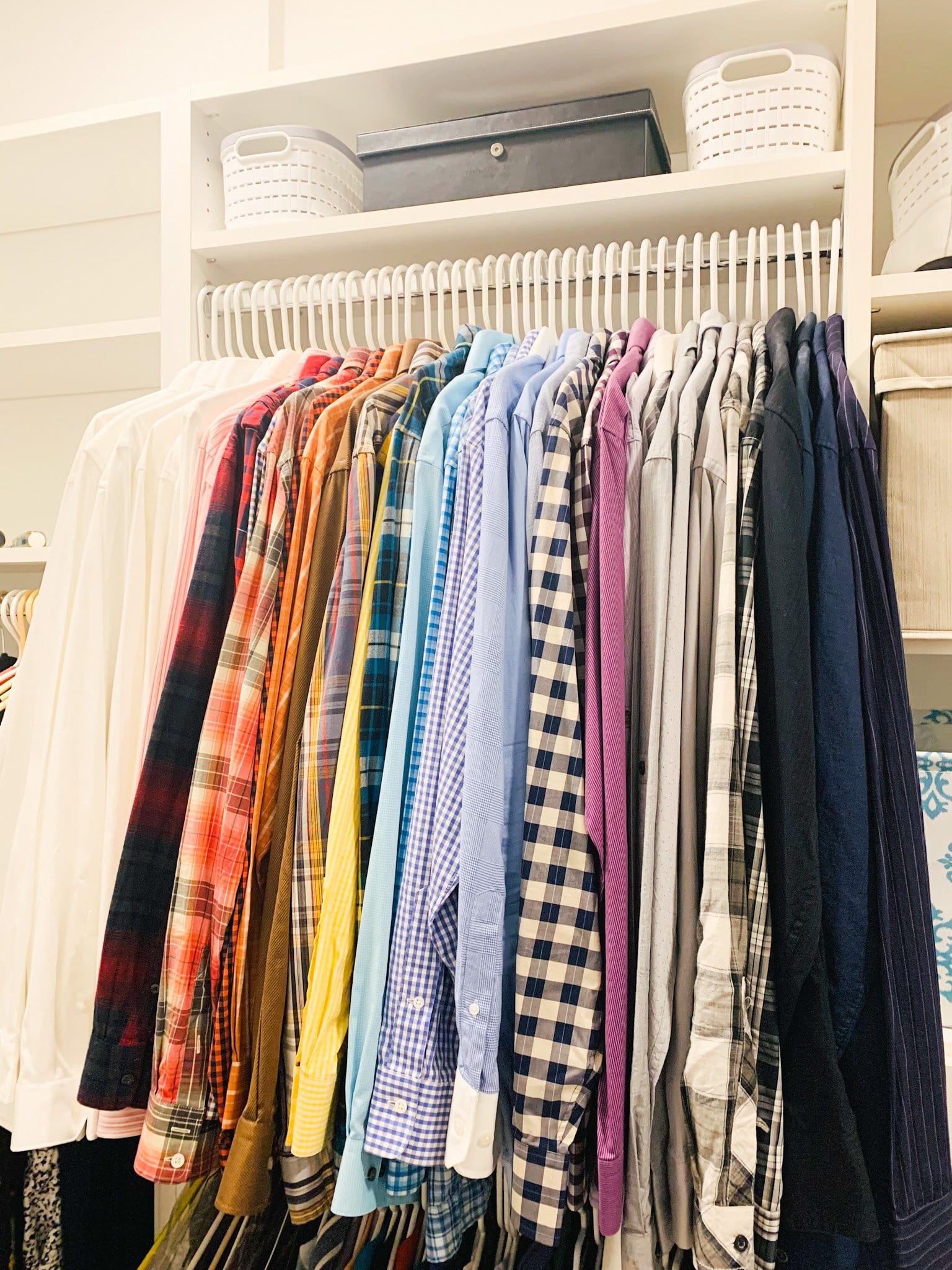 Closet rod of button-up shirts organized in rainbow colour order