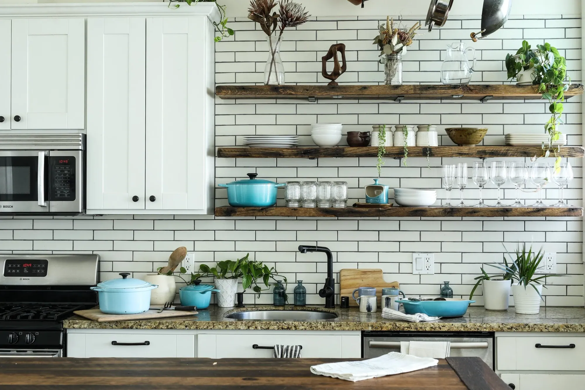 Bright white kitchen with wood open shelving and turquoise cookware